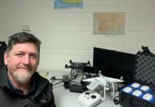 Drone flyer diary: Mathew Hilyard Photograph shows a man beside a white quadcopter drone, remote controller, batteries, monitors, and related equipment.